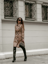 a lady in a gathered waist double-breasted trench coat with knee-high boots
